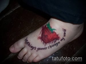 Фото татуировки клубники с цитатой 'Nothing's gonna change my world' на лодыжке. Оригинальный и стильный рисунок татуировки.