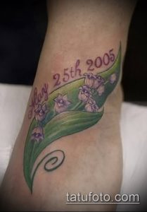 Фото тату: изящные ландыши с подписью 'Mary 25th 2005' на запястье, выполненные в мягких фиолетовых и зеленых тонах.