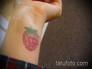 Фото тату: небольшая, акварельная татуировка с изображением ягоды малины и зеленых листьев на запястье.