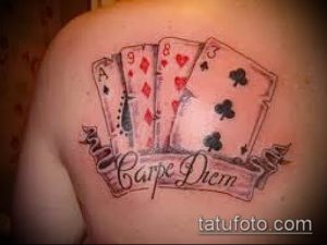 Фото татуировки на плече: четыре игральные карты и надпись 'Carpe Diem' на ленте. Рисунок татуировки в стиле традишнл.