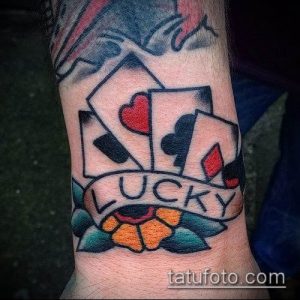 Фото тату с игральными картами и надписью "Lucky" на предплечье. Яркий рисунок татуировки в стиле олдскул с цветами.