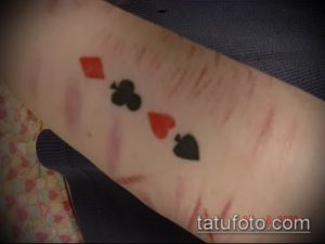 Фото тату с изображением четырех карточных мастей (черви, трефы, пики, бубны) в минималистичном стиле на предплечье. Масти выполнены в красном и черном цветах.
