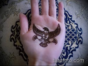 Фото тату: изящная коричневая мехенди птица с расправленными крыльями на женской ладони, украшенная точками.