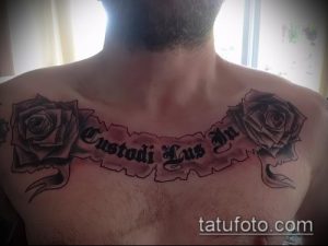 Фото тату на груди мужчины: две розы с шипами и надпись на латыни "Custodi Lus In". Татуировка выполнена в черно-серых тонах.