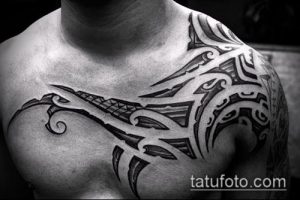 Фото тату: черная татуировка в стиле трайбл, покрывающая плечо и часть груди мужчины. Сложный геометрический рисунок татуировки.