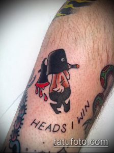 Фото тату на руке с изображением скелета с топором и надписью "HEADS I WIN", выполненное в стиле old school с яркими цветами и четкими контурами.
