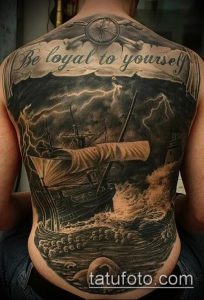Фото тату корабля в шторме на спине с компасом и надписью "Be loyal to yourself". Детализированный черно-серый рисунок.