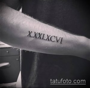 Фото тату: римские цифры X.XXI.XCVII на руке мужчины, черный цвет, тонкие линии, минималистичный дизайн, лаконичная татуировка.