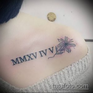 Фото тату: римские цифры MMXXV IV V и цветок на плече девушки, тонкие линии, черный цвет, минималистичный дизайн, нежная татуировка.