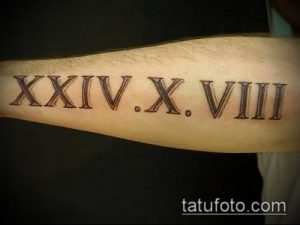 Фото тату: римские цифры 'XXIV.X.VIII' на мужском предплечье, выполненные в классическом стиле черными чернилами. Четкий и выразительный рисунок татуировки.