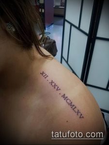 Фото тату: черные римские цифры 'XII. XXV. MCMLXV' на женском плече, выполненные четкими линиями. Минималистичный дизайн, подходящий для тех, кто ценит лаконичность.