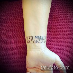 Фото татуировки на запястье с римскими цифрами V VII MMXIV и декоративным узором. Элегантный и женственный дизайн.