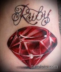 Фото тату рубина с надписью 'Ruby' на женской руке. Яркий красный драгоценный камень с реалистичными гранями и бликами.