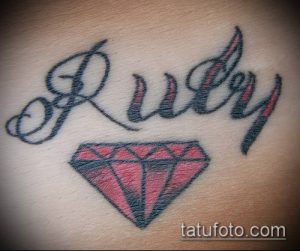 Фото тату: небольшой бриллиант и надпись "Ruby" на руке. Простой и стильный рисунок татуировки в минималистичном стиле.