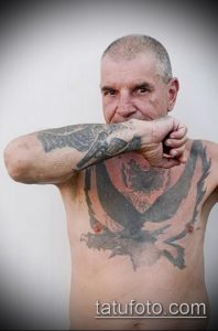 Фото тату: изображение дракона и ворона на груди и руке мужчины. Черно-серые тона, реалистичный стиль, детализированный рисунок.