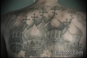 Фото тату на спине, изображающее православные храмы с крестами. Детализированный рисунок в серо-черных тонах, символизирующий веру и духовность.