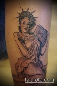 Фото тату на руке с изображением Статуи Свободы, держащей книгу. Рисунок выполнен в черно-серых тонах с акцентом на детализацию лица и драпировки.