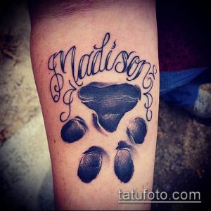 Фото тату на предплечье: черная лапа собаки с надписью 'Madison' в каллиграфическом стиле. Изящный рисунок татуировки для любителей животных.