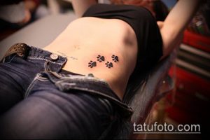 Фото тату: Три маленьких черных отпечатка лап на боку. Нежный и минималистичный дизайн, подходящий для девушек.