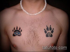 Фото тату двух черных отпечатков лап на груди мужчины. Симметричный рисунок, выполненный в минималистичном стиле.