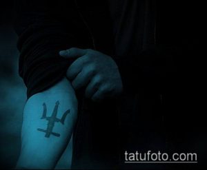 Фото минималистичной татуировки трезубца на локте. Простой чёрный рисунок, символизирующий власть и силу.