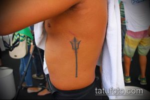 Фото тату: простой и элегантный тризуб на боку, выполненный тонкими линиями. Минималистичный дизайн и аккуратная проработка.