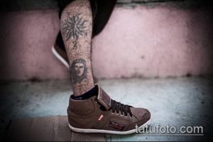 Фото тату: портрет Че Гевары на икре с цветочными узорами и кедами, выполненный в черно-серых тонах.