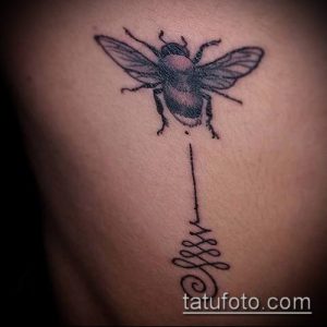 Фото татуировки пчелы над символом Ом на боку. Черно-белый рисунок с тонкими линиями и детальной проработкой.