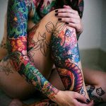 Фотография женского рукава, полностью покрытого яркими цветочными татуировками. Изображены лотосы, розы и другие цветы в ярких цветах.