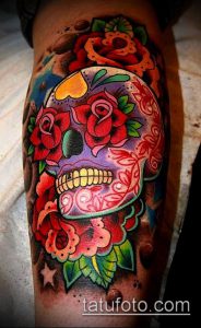Фото татуировки в стиле Day of the Dead с изображением черепа, украшенного розами и другими цветами. Яркие цвета и детализированная проработка.