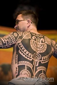 Фото тату: сложный полинезийский узор, покрывающий всю спину и руки мужчины. Черные линии на светлой коже, детальная проработка.