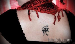 Фото татуировки Глаза Гора на спине девушки. Миниатюрный рисунок в черных тонах, расположенный между лопатками.