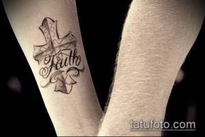Фото тату креста с надписью 'Faith' на руке. Черно-белый рисунок татуировки с каллиграфическим шрифтом и декоративными элементами.