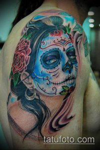Фото тату женского лица в стиле Sugar Skull на плече. Голубые и розовые оттенки, цветочные элементы, детальная прорисовка.