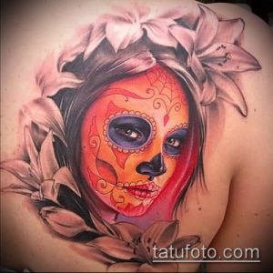 Фото татуировки в стиле Sugar Skull на лопатке. Изображение женского черепа, украшенного цветами и ярким макияжем.