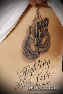 Фото тату на боку: реалистичные боксерские перчатки и надпись 'Fighting for Love' выполнены в черно-серых тонах.