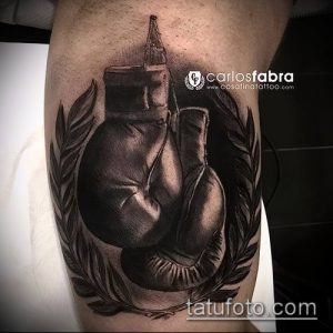 Фото тату: черно-серая татуировка боксерских перчаток, окруженных лавровым венком, на предплечье.