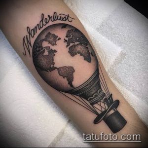 Фото тату на предплечье: воздушный шар в виде глобуса с надписью 'Wanderlust'. Детализированный рисунок в стиле реализм.