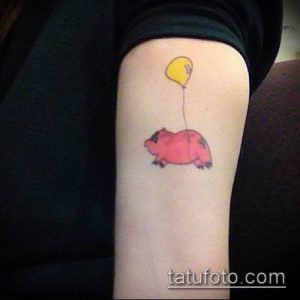 Фото татуировки на предплечье с изображением розового поросенка, держащего желтый воздушный шар.
