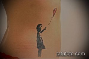 Фото тату: татуировка в стиле стрит-арт с изображением девочки, отпускающей воздушный шар. Черно-белый рисунок на боку.