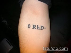 Фото тату на руке: простая надпись 0 RhD-. Лаконичный и информативный дизайн.
