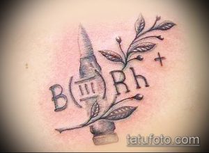 Фото татуировки с изображением группы крови B(III)Rh, ветки с листьями и небольшого креста, выполненной в серо-черных тонах.