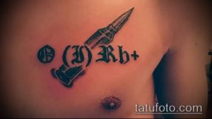 Фото татуировки с изображением группы крови B(III)Rh+ и копья, выполненной в черных тонах на теле.