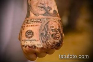 Фото татуировки на руке с реалистичным портретом Бенджамина Франклина на долларовой купюре. Детализированный рисунок в черно-серых тонах.