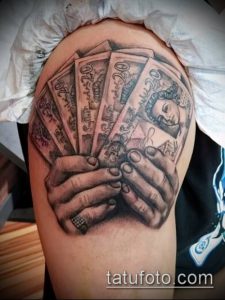 Фото тату на плече с изображением рук, держащих пачку банкнот. Реалистичный рисунок с использованием черных и серых оттенков.