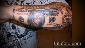 Фото тату: изображение банкноты в 100 долларов с портретом Бенджамина Франклина и элементами дизайна, выполненное на руке.