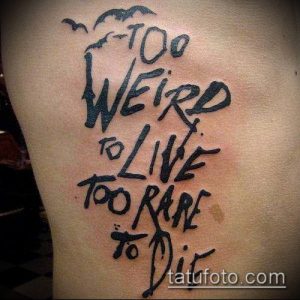 Фото тату: надпись "Too Weird to Live Too Rare to Die" в стилизованном шрифте на боку. Чёрные чернила, небрежный стиль.