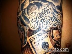 Фото тату на руке: изображение долларовой купюры с именем "Jaden Eurroe", украшенное витиеватыми узорами и декоративными элементами. Черно-серые тона.