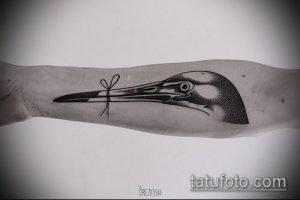 Фото минималистичной татуировки головы аиста на руке. Черно-белый рисунок с четкими линиями и небольшим бантиком. Эскиз тату.