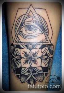 Черно-белое фото татуировки с изображением Всевидящего Ока в треугольнике и цветка. Детализированный рисунок с геометрическими элементами.